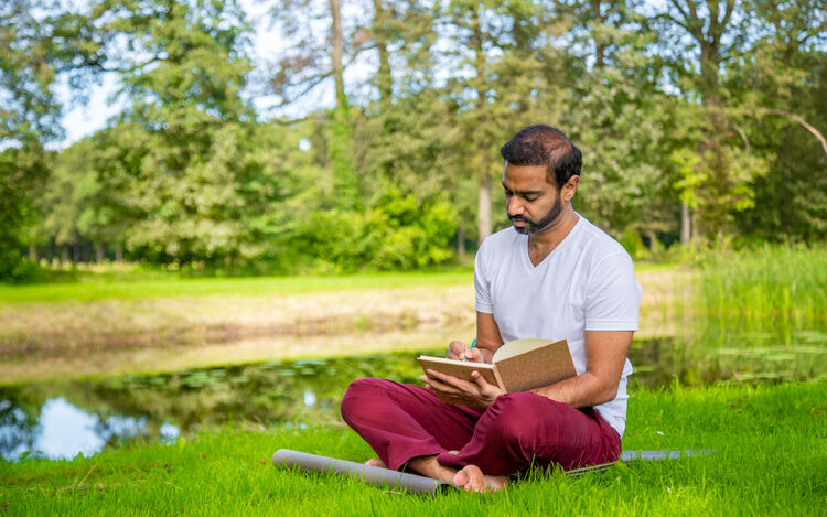 Yoga teacher in Sukhasana or easy pose, self-reflecting in a natural surrounding Yoga Teacher sitting in Sukhasana in nature and journaling