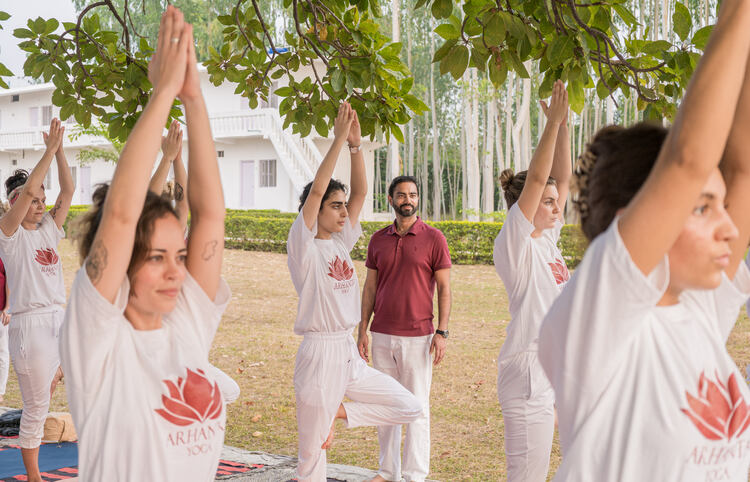Students practicing Vrksasana or tree pose under the teacher’s guidance Yoga teacher guiding students in Tree pose