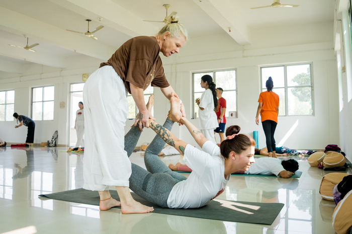 A yoga teacher adjusts a student’s pose during a yoga retreat A yoga teacher adjusts a student’s pose during a yoga retreat