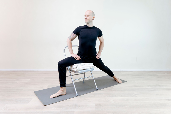 A man practices Warrior Pose with the support of a chair