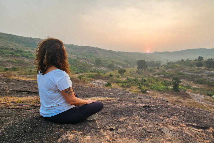 Woman meditating alone in the Sukhasana easy pose on a rocky hilltop