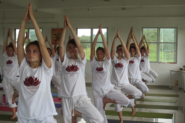 Class of yoga students learning tree pose in traditional setting