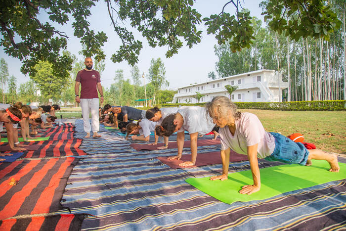 Yoga teacher guiding students through a pose outside ashram 